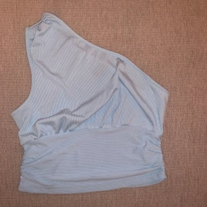 Ljusblå randig oneshoulder topp - Säljer en superfin ljusblå oneshoulder topp med smala ränder. Toppen är i ett mjukt och bekvämt material. Från shein i storlek S, aldrig använd 