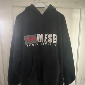 Svart hoodie från Diesel - Säljer en svart hoodie från Diesel med stort tryck på framsidan. Den är superbekväm och perfekt för kyliga dagar. Hoodien har en klassisk passform med långa ärmar och en stor ficka framtill. Perfekt för både vardag och chill! 🖤
