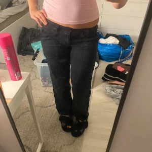 Svarta byxor - Snygga svarta byxor med låg midja och rak passform. Perfekta för en avslappnad stil. De har en klassisk design med knappar och dragkedja framtill.