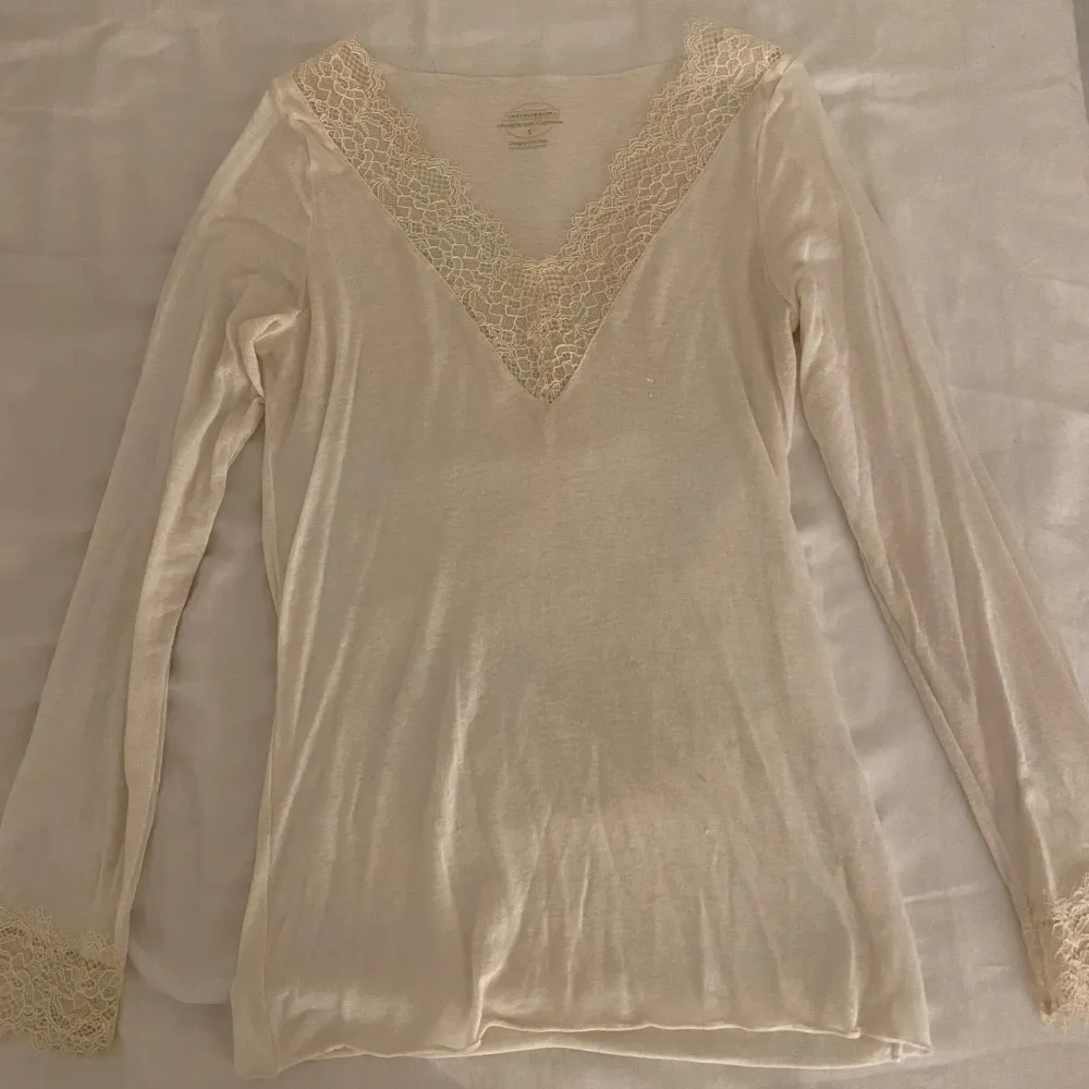Säljer en elegant beige/Vit långärmad topp från Intimissimi. Toppen har en vacker spetsdetalj vid v-ringningen och ärmsluten. Den är sällan använd och är i bra skick. Neuletakit & Villapaidat.