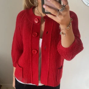 Röd stickad kofta från East West - Säljer en snygg röd stickad kofta från East West med stora knappar framtill. Ribbad och har trekvartsärmar!