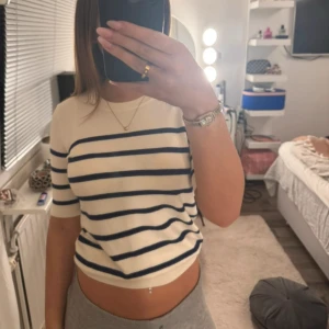 Stickad topp från Zara - Säljer en stilren vit randig topp med korta ärmar från Zara. Den är stickad. Toppen är croppad och passar perfekt för en avslappnad look. Storlek S, men passar mer som en xs. 