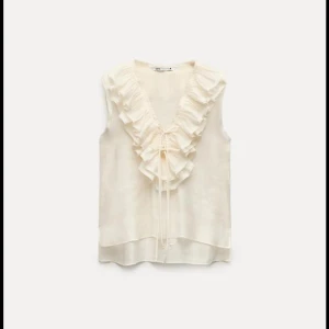 Beige/gul ärmlös blus från Zara - Säljer en elegant beige/gul ärmlös blus från Zara med volangdetaljer och knytning framtill. Perfekt för en stilren look. Använd 1 gång. Färgen syns bäst i de 3 sista bilderna!💛💛 kan absolut tänka mig gå ner i pris vid snabb affär!