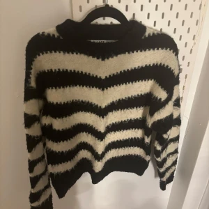 Svart och vit randig stickad tröja - Säljer en mysig stickad tröja i svart och vitt med ett randigt mönster. Tröjan har långa ärmar och en rund halsringning. Perfekt för kyliga dagar!