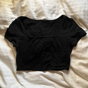Svart croppad topp - Säljer en stilren svart croppad topp med korta ärmar. Perfekt för en trendig look. Toppen har en fyrkantig halsringning som ger en modern touch.