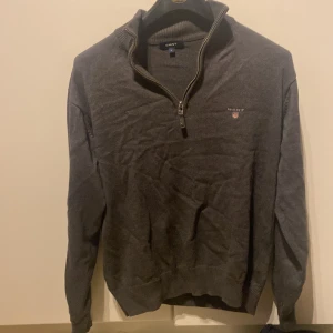 Grå tröja med dragkedja från GANT - Säljer en stilren grå tröja från GANT med dragkedja och ribbad krage. Perfekt för kyligare dagar och passar bra till både jeans och chinos. Tröjan har en diskret logga på bröstet.