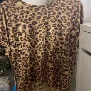 Leopardmönstrad t-shirt - Säljer en leopardmönstrad t-shirt i ett mjukt och bekvämt material. T-shirten har korta ärmar och en rund halsringning. Perfekt för att lägga till lite djurmönster i din garderob!