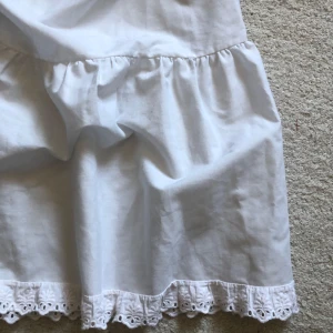 Vit kjol med spetsdetaljer - Säker denna jättegulliga vit kjol med elastisk midja och volangdetaljer. Kjolen har en söt spetskant längst ner. Perfekt för en somrig look.