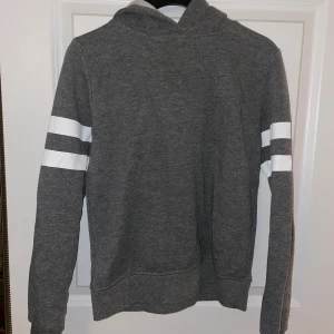 Grå hoodie - En grå hoodie från gina tricot med vita ränder runt armarna och en huva. Säljer pga den inte passar mig längre annars jättebra skick