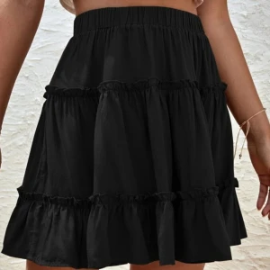 Svart volangkjol - OANVÄND  - Trendig svart kortkjol med volanger och elastisk midja. Perfekt för att skapa en stilren look med en touch av elegans. Helt oanvänd!