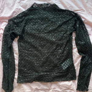Svart paljettopp från Gina Tricot - Snygg svart topp från Gina Tricot täckt med glittrande paljetter i ett rutmönster. Perfekt för en kväll ute eller festliga tillfällen. Toppen har långa ärmar och en tight passform som framhäver figuren.