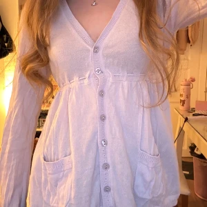 Ljuslila babydoll kofta  - Säljer en söt ljuslila babydoll kofta från EastWest med knappar framtill och knytband i ryggen. Koftan har långa ärmar och två fickor fram. Stl M men passar S mer, öppen för prisförslag 😊💗