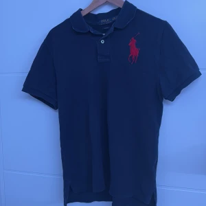 Svart pikétröja från Ralph Lauren - Säljer en stilren svart pikétröja från Ralph Lauren med röd broderad logga på bröstet och siffran 3 på ärmen. Tröjan är i slim fit och har korta ärmar. Perfekt för en avslappnad men ändå snygg look. Tröjan är i storlek M men passar S 