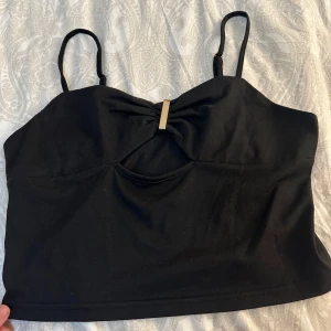 Svart linnetopp med gulddetalj - Snygg svart linnetopp med smala axelband och en elegant gulddetalj framtill. Perfekt för en stilren look.