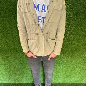 Fieldjacka - Snygg beige parkajacka med dragkedja och knappar. Jackan har flera praktiska fickor och en avslappnad passform. Perfekt för höst och vår.