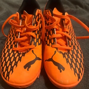 Orange fotbollsskor från Puma - KNAPPT ANVÄNDA! Skorna blev snabbt små. Snygga orange fotbollsskor från Puma med svart mönster och snörning. Skorna har en slitstark sula med bra grepp och är perfekta för fotbollsträning. Den ikoniska Puma-loggan syns tydligt på sidan och sulan.