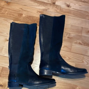 Svarta stövlar Mexx med dragkedja - Snygga svarta stövlar i skinn med dragkedja på baksidan. Perfekta för höst och vinter. De har en klassisk design med rund tå och låg klack, vilket gör dem både stiliga och bekväma.