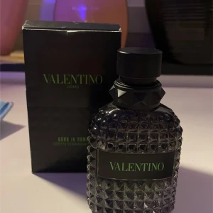 Valentino Uomo Born in Roma - Säljer en elegant parfymflaska från Valentino, Uomo Born in Roma. Flaskan har en lyxig design med ett mönstrat glas och svart kork. Perfekt för den som vill ha en sofistikerad doftupplevelse.