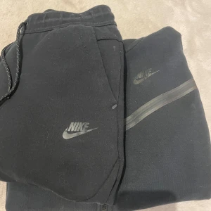 Svart hoodie och byxor från Nike - Säljer en svart hoodie och matchande byxor från Nike. Koftan är i användt skick och har skrapor på sig. Byxorna är i bättre skick som inte är använda lite mycket för att dom var för korta för mig. Går att få fler bilder. Och går att köpa en för en då priset kan diskuteras.