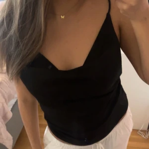 Svart linne med smala axelband från GinaTricot - Snyggt svart linne från GinaTricot. Toppen har  smala axelband och urringning och är även låg i ryggen. Perfekt för en middag eller fest. Passar bra till både byxor och kjol. Säljer då den är för stor på mig. Endast använd 1 gång innan.