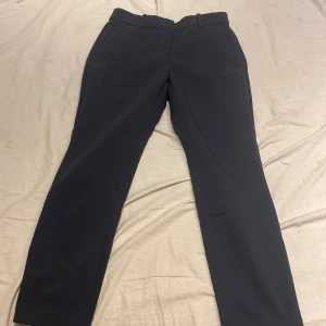 Mörk blåa kostymbyxor - Snygga mörk blåa kostymbyxor med en klassisk design. De har en rak passform och är perfekta för en stilren look. Byxorna har en diskret dragkedja och knapp framtill.