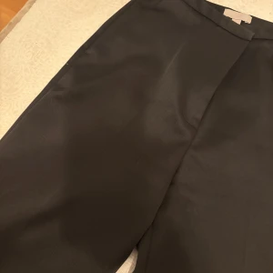 Svarta silkes kostymbyxor från H&M - Snygga svarta silkes  kostymbyxor från H&M med en klassisk design. Byxorna har en rak passform och är tillverkade i ett elegant material som ger en stilren look. Perfekta för en formell outfit. Stl 36
