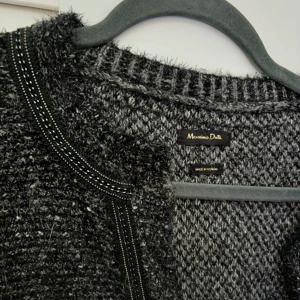 Svart stickad kavaj från Massimo Dutti - Snygg svart stickad kavaj från Massimo Dutti med subtila detaljer och fickor framtill. Perfekt för en stilren look. Den har en öppen design utan knappar och långa ärmar.