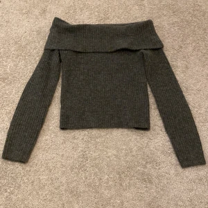Grå offshoulder tröja från H&M - Jättefin mörkgrå off-shoulder tröja från H&M med prislappen kvar! Tröjan är ribbad och har långa ärmar. Passar till både jeans och kjol. Perfekt för höst och vinter!