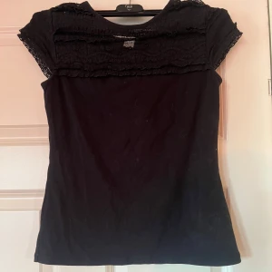 Svart topp med spetsdetaljer -  svart topp med spetsdetaljer på axlar och över bröstet.  Så så fin 