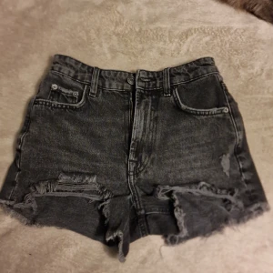 Svarta jeansshorts från Zara - Snygga svarta jeansshorts från Zara med fransiga kanter och en cool, sliten look. Perfekta för en avslappnad stil. De har fem fickor och knappgylf.