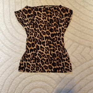 Leopardmönstrad topp - Snygg leopardmönstrad topp med korta ärmar och båt krage. Toppen har en figurnära passform och är tillverkad i ett mjukt material. 