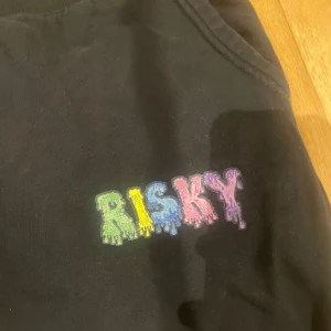 Svarta mjukisbyxor med färgglatt tryck - Säljer ett par svarta mjukisbyxor med ett färgglatt 'RISKY' tryck på framsidan. Byxorna har snörning i midjan och en bakficka. Perfekta för en avslappnad stil.