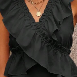 Svart blus med volangdetaljer - Snygg svart blus med volangdetaljer och djup v-ringning. Perfekt för en stilren look med en touch av elegans. Storlek M men passar även för folk som har storlek S