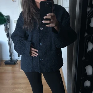 Mörkblå teddyjacka med knappar - Mysig mörkblå teddyjacka med stora knappar framtill. Jackan har en oversized passform och långa ärmar, perfekt för kyligare dagar. Den har också praktiska fickor på sidorna.