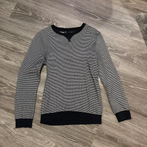 Svartvit tröja från Cubus - Säljer en svartvit tröja från märket Cubus. Tröjan har ett diskret rutmönster och svarta ribbade muddar vid ärmslut och nederkant. Perfekt för en stilren look.