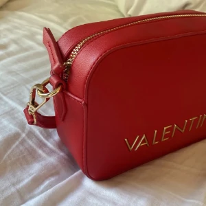 Röd axelväska från Valentino - Snygg röd axelväska från Valentino. Väskan har en justerbar axelrem och dragkedja upptill. Den är köpt på zalando för 1299kr men jag säljer för 499kr. Den är endast använd max 3gånger, ser ut som ny! Pris kan diskuteras! 