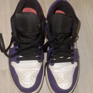 Nike Air Jordans i lila och svart - Säljer ett par Nike Air Jordans i lila och svart med vita detaljer. Skorna har snörning och en klassisk design med perforerad tå för ventilation. Perfekta för dig som älskar sneakers med stil.