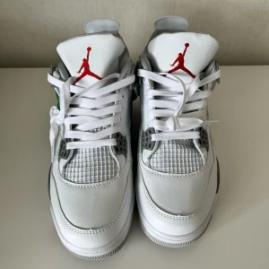 Jordan 4 Retro Oreo - Snygga Nike Air Jordans i vitt med grå detaljer och röd logga. Skorna har snörning och en stilren design med synlig luftdämpning i sulan. Perfekta för dig som vill ha både stil och komfort.