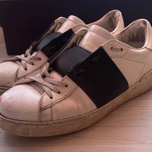 Valentino sneakers med svart detalj - Snygga Valentino sneakers i beige med en bred svart detalj över snörningen. Skorna har en klassisk design med rund tå och platt sula. Perfekta för en stilren look. Sulan har släppt i framkant men kan lösas enkelt hos en skomakare. Allt og Cond:6/10