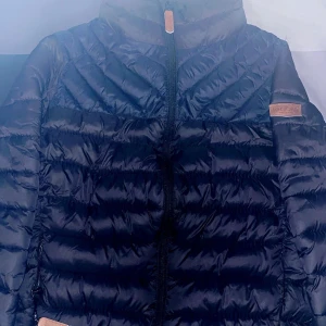 Svart dunjacka från Kayoba - Snygg svart dunjacka från Kayoba i storlek S. Jackan har en quiltad design med dragkedja framtill och hög krage för extra värme. Perfekt för kyliga dagar.