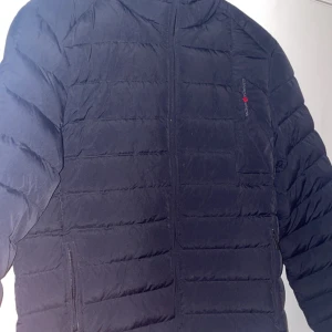 Canada Snow Lucas Jacket Navy - Snygg mörkblå jacka med dragkedja framtill. Jackan har en quiltad design och är perfekt för kyligare väder. Den har en hög krage för extra värme och stil. Ordinarie pris 2400kr, nypris 700kr