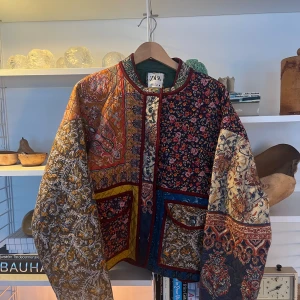 Färgglad quiltad jacka från Zara - Unik och färgglad quiltad jacka från Zara med ett mixat blommigt mönster. Jackan har långa ärmar och flera fickor med knappar. Jackan är i storlek 40. Den saknar knappen längst ned. Den är väldigt eftertraktad därav priset.