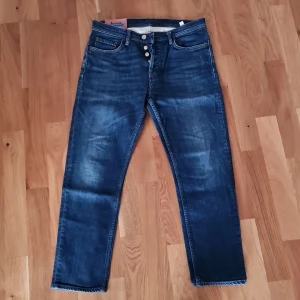 Acne River jeans 29/30 - Snygga mörkblå jeans från Acne Studios i modellen River Dark Blue. Tillverkade i Italien med en klassisk femficksdesign och knappgylf. Perfekta för en stilren look.
