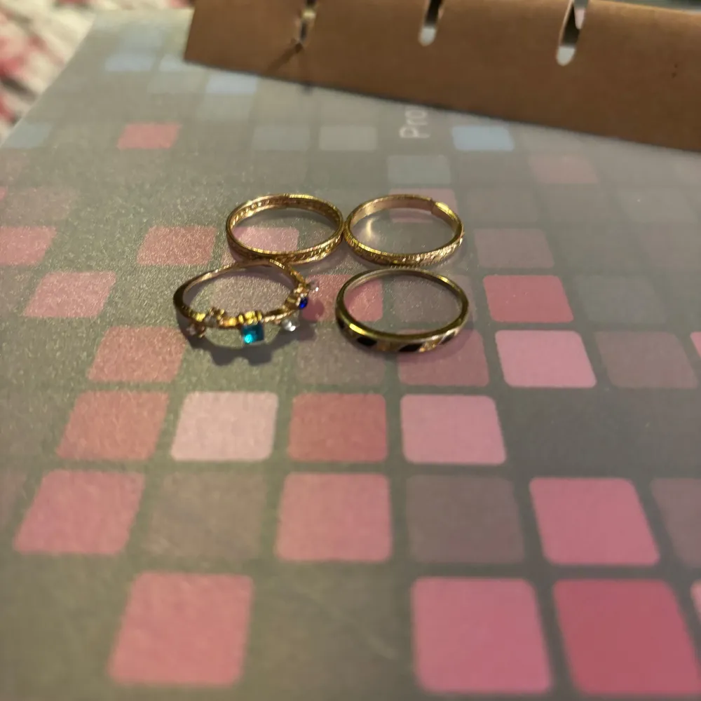 Fyra stilrena guldiga ringar, varav en är dekorerad med färgglada pärlor i blått och rosa. Perfekta för att lägga till en touch av färg och elegans till din stil.. Asusteet.