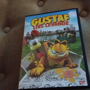 Gustaf - Livs Levande DVD - DVD med filmen 'Gustaf - Livs Levande'. Omslaget visar Gustaf och en annan karaktär framför en stadsmiljö. Texten 'Alla talar svenska' finns på framsidan.