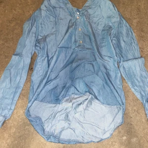 Blå henley-skjorta - Snygg blå henley-skjorta med knappar framtill. Skjortan har långa ärmar. Tillverkad i ett lätt och bekvämt material.