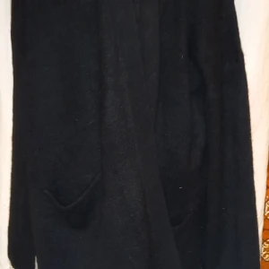 Svart cardigan - Säljer en stilren svart cardigan i mjukt material. Perfekt för lager-på-lager under kyliga dagar. Den har långa ärmar och praktiska fickor framtill. Helt ny med prislapp kvar