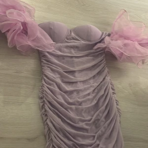 Lila klänning med volangärmar - Säljer en fantastisk lila klänning med dramatiska volangärmar. Klänningen har en tight passform och är tillverkad i ett syntetmaterial som ger en smickrande siluett. Perfekt för speciella tillfällen!