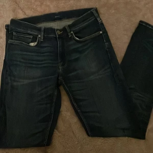 Mörkblå jeans från Gant - Snygga mörkblå jeans från Gant med klassisk femficksdesign och knappgylf. Perfekta för en stilren look. Passar både till vardags och mer uppklädda tillfällen.