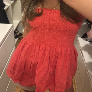 Röd axelbandslös topp - Kan användas som en fin volang topp, men även en kjol🌸En söt röd/orange axelbandslös topp med smockdetaljer upptill och en luftig kjol. Perfekt för varma sommardagar. Toppen har en härlig färg och en bekväm passform.